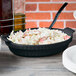 A black Tablecraft shallow oval casserole dish with food inside.