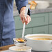A person using a Vollrath stainless steel ladle to serve soup.