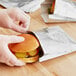 A person in gloves putting a hamburger in a Carnival King foil sandwich bag.