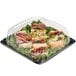 A Sabert plastic catering tray with sandwiches and greens in it.