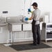 A man wearing blue gloves washing dishes in a Regency 3 compartment commercial sink.