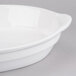 A Tablecraft white cast aluminum oval casserole dish with a handle.