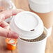 A hand holding a white plastic lid on a coffee cup.