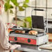 A woman cooking meat and cheese sandwiches on an Avantco commercial panini grill.