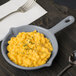 A Tablecraft gray cast aluminum fry pan filled with macaroni and cheese on a table with a fork and spoon.