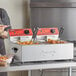 A woman standing next to an Avantco dual tank electric countertop fryer.