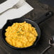 A Tablecraft black and green speckled cast aluminum fry pan filled with macaroni and cheese on a table.