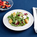 An Arcoroc vintage porcelain salad plate with salad and fruit on it.