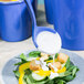 A Tablecraft blue speckle long ladle pouring dressing on a salad.