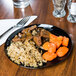 A WNA Comet black plastic plate with rice and meat on a table