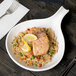 A Tablecraft white cast aluminum skillet with food on a table.