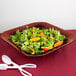 A salad with carrots and lettuce in a maroon speckled square bowl with a spoon and fork.