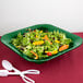 A green Tablecraft square bowl filled with salad and orange vegetables.