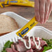 A hand holding a yellow Hellmann's Mayonnaise packet over a sandwich.