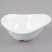 A white Tablecraft melamine bowl with a curved wavy shape on a gray surface.