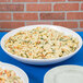 A Tablecraft white cast aluminum pasta bowl filled with pasta and vegetables on a table.