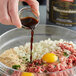 A hand pouring Worcestershire sauce into a bowl of food.