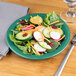 A Carlisle meadow green melamine salad plate with salad on it.