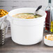 A white Tablecraft bain marie bowl filled with soup on a white pot.