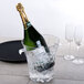 A bottle of champagne in a Thunder Group polycarbonate wine bucket on a table with a glass of ice.