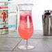 A Thunder Group plastic hurricane glass filled with a pink drink and ice on a table near a bottle of alcohol.