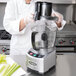 A woman in a white coat using a silver and black Waring food processor on a counter in a professional kitchen.