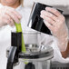 A person in gloves using a Waring food processor to make a vegetable juice.