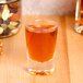 A Thunder Group reusable plastic shot glass filled with nuts and brown liquid on a table in a bar.