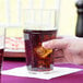 A person holding a Thunder Group clear polycarbonate tumbler filled with soda.