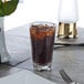 A Thunder Group plastic pint glass filled with brown liquid and ice sits on a table.
