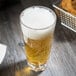A Thunder Group plastic mixing glass with beer and foam on top on a table.