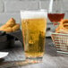 A Thunder Group plastic mixing glass filled with brown liquid sits on a table next to a plate of food.