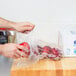 A hand holding an apple in an Inteplast Group plastic bag on a wooden surface.