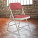 A close-up of a National Public Seating gray metal folding chair with a red padded seat.