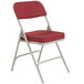 A gray metal folding chair with a new burgundy fabric padded seat.