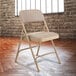 A beige National Public Seating metal folding chair with a padded seat sitting on a wooden floor.