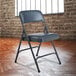 A National Public Seating black metal folding chair with dark midnight blue vinyl padding.