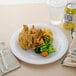 A Carlisle white melamine plate with food on a white table.