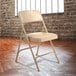 A tan National Public Seating metal folding chair with a French beige padded seat.