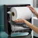 A large white hardwound paper towel roll being placed into a black wall-mounted dispenser.