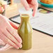 A hand pouring green liquid into a Cambro Camliter beverage decanter with a lid.