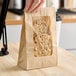 A brown kraft paper bag with a clear polyethylene window displaying two cookies inside.