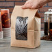 A hand holding a Choice brown Kraft paper bag filled with coffee beans.