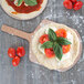 A pizza with tomatoes and basil on a pizza peel.