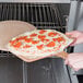 A person using an American Metalcraft pizza peel to put a pizza in the oven.