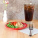 A red Sensation wide rim melamine plate with rice and vegetables on a table.