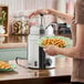 A stainless steel topping warmer and pump dispenser being used to pour syrup onto waffles.