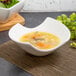 A white porcelain bowl of soup with noodles and carrots on a placemat.