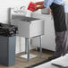 A person in a black apron pouring water into a Steelton commercial utility sink.