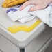 A hand wipes a table with a gray Metro utility cart in the background.